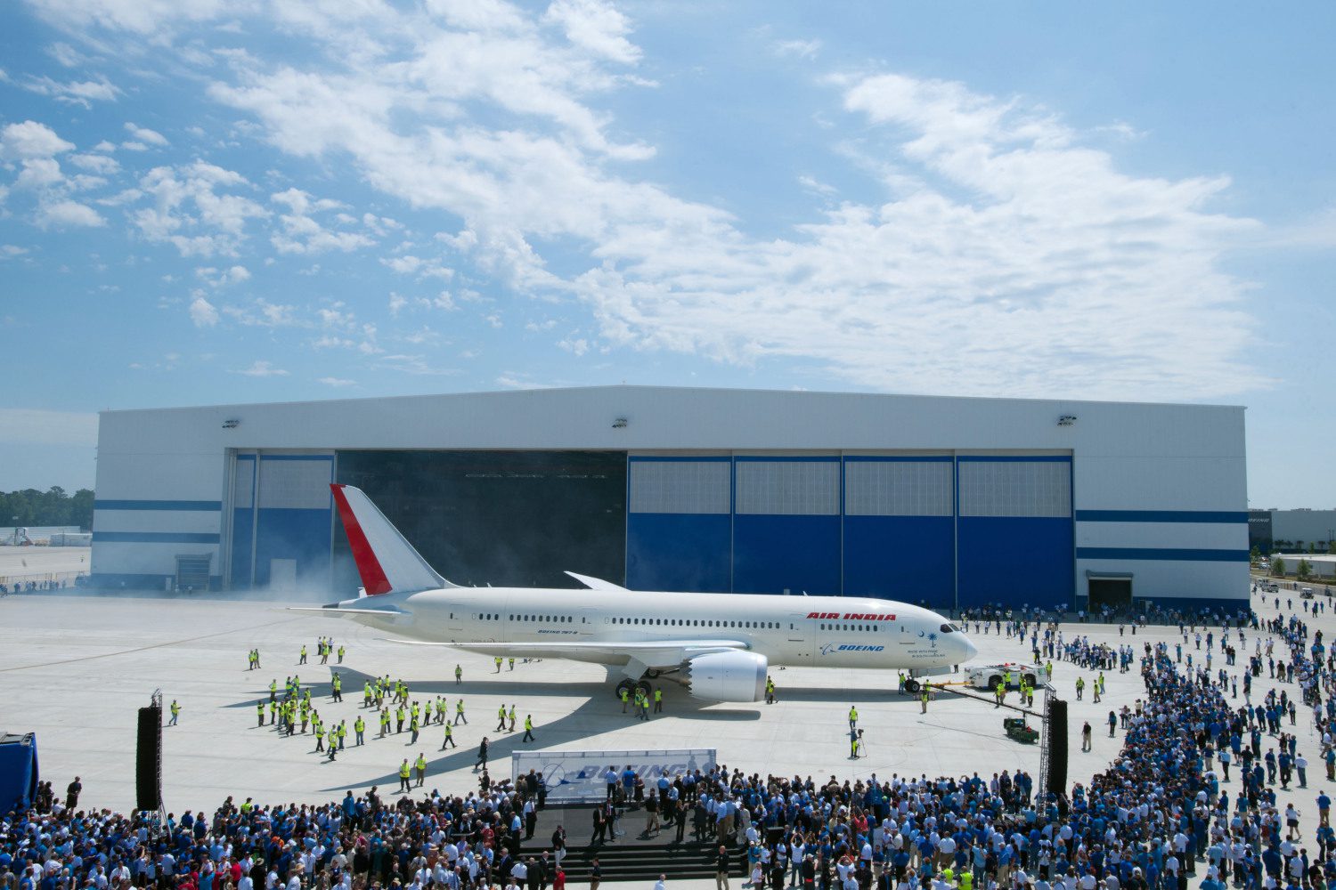 Gray and blue hangar with white plane and crowd