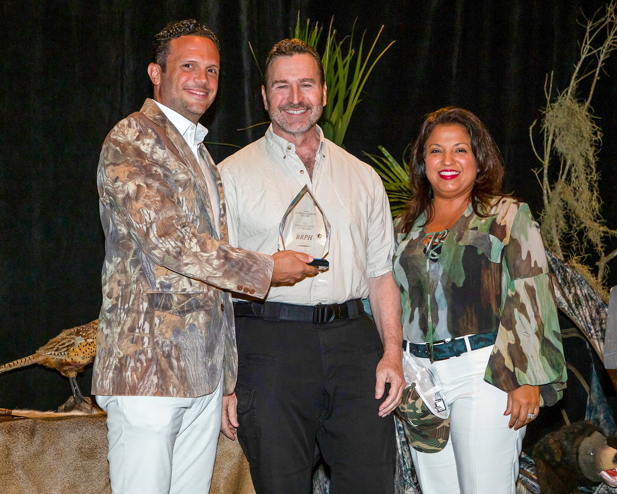 Man in white shirt accepting clear award from man in camo jacket