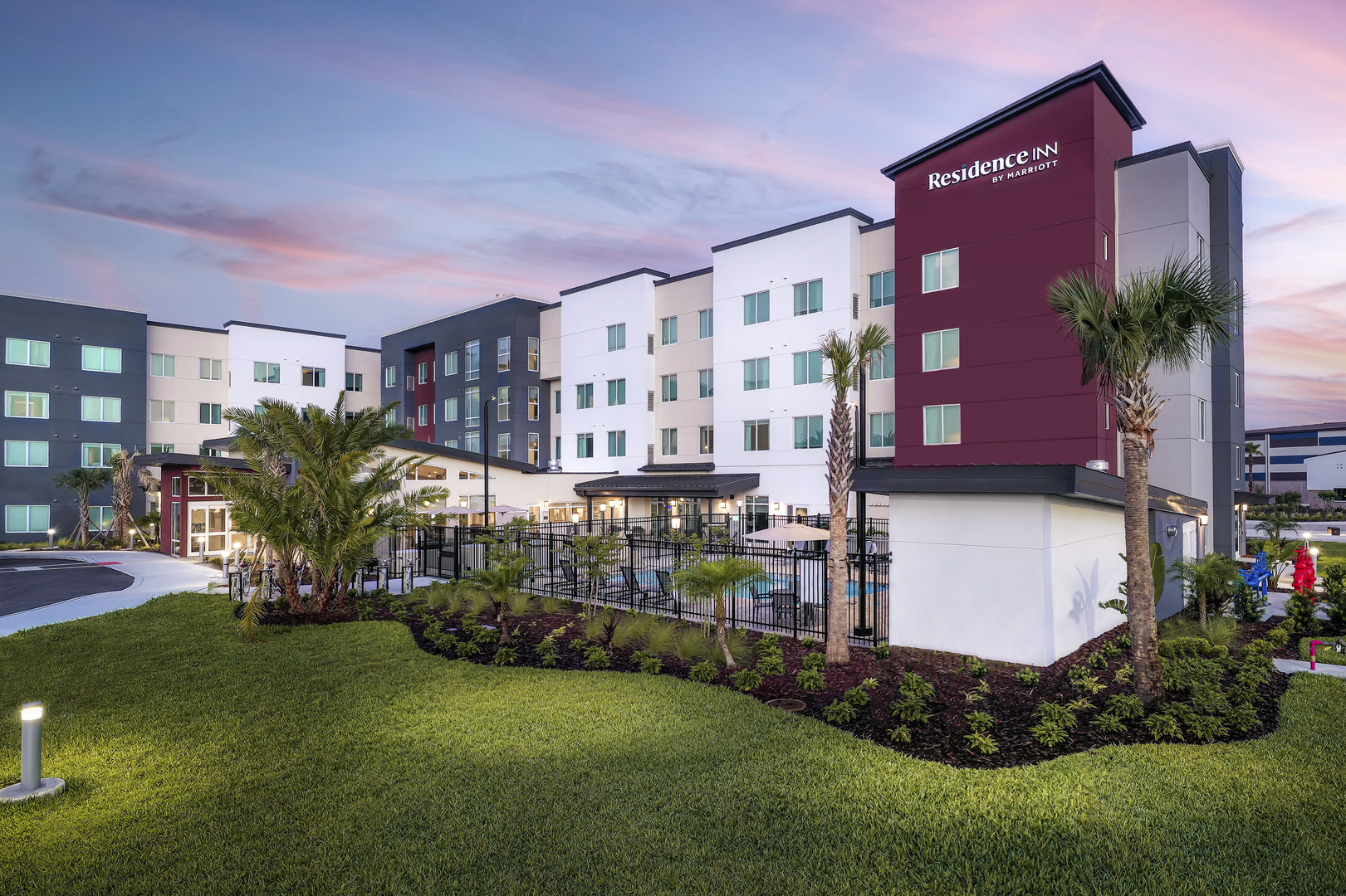 Ext white, purple, gray hotel with green landscape in front
