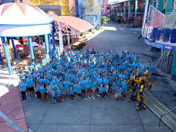 large group of BRPH employees who are all wearing blue t-shirts standing together at Universal City Walk near the Bumble Bee Transformer statue