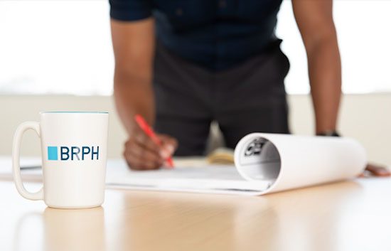 Man writing on a building plan with red pen on a table featuring a coffee cup with the BRPH logo on it