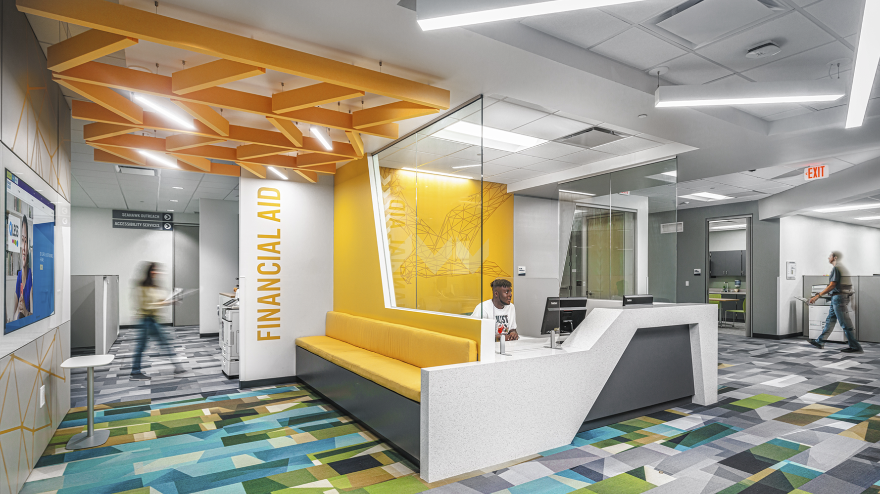 Lobby with multi colored checkered carpet with white and orange ceiling and yellow couch against white desk. Financial Aid is in yellow on white wall