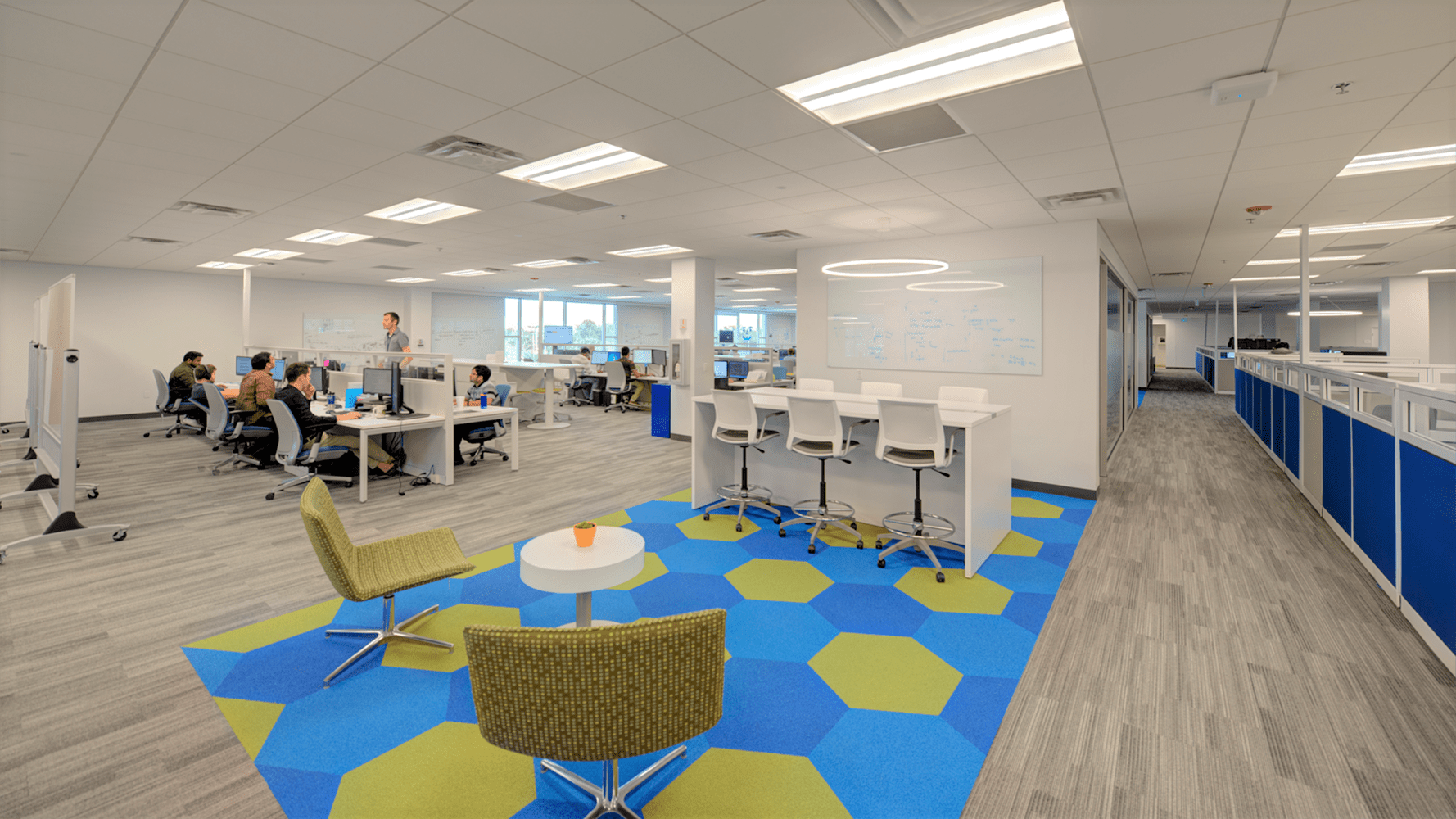 room with gray floors, blue cubicles, white chairs, and blue/yellow rug