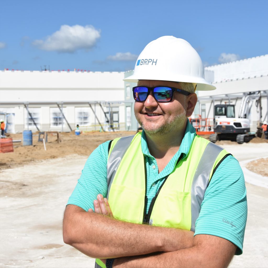 Man with turquoise shirt and yellow vest with white hardhat