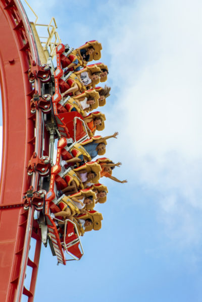 People riding on roller coaster hanging vertically against blue sky