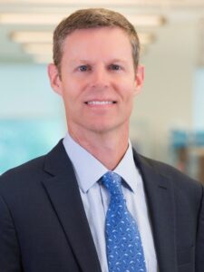 Man in jacket with blue tie smiling at camera.