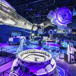 Space capsules and rockets displayed indoors with purple lighting.